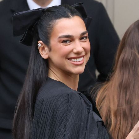 Dua Lipa smiles at the camera wearing a black hair bow