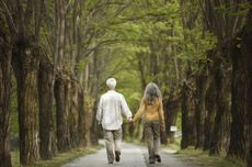 Senior couple walking hand in hand on a tree-lined road, Italy