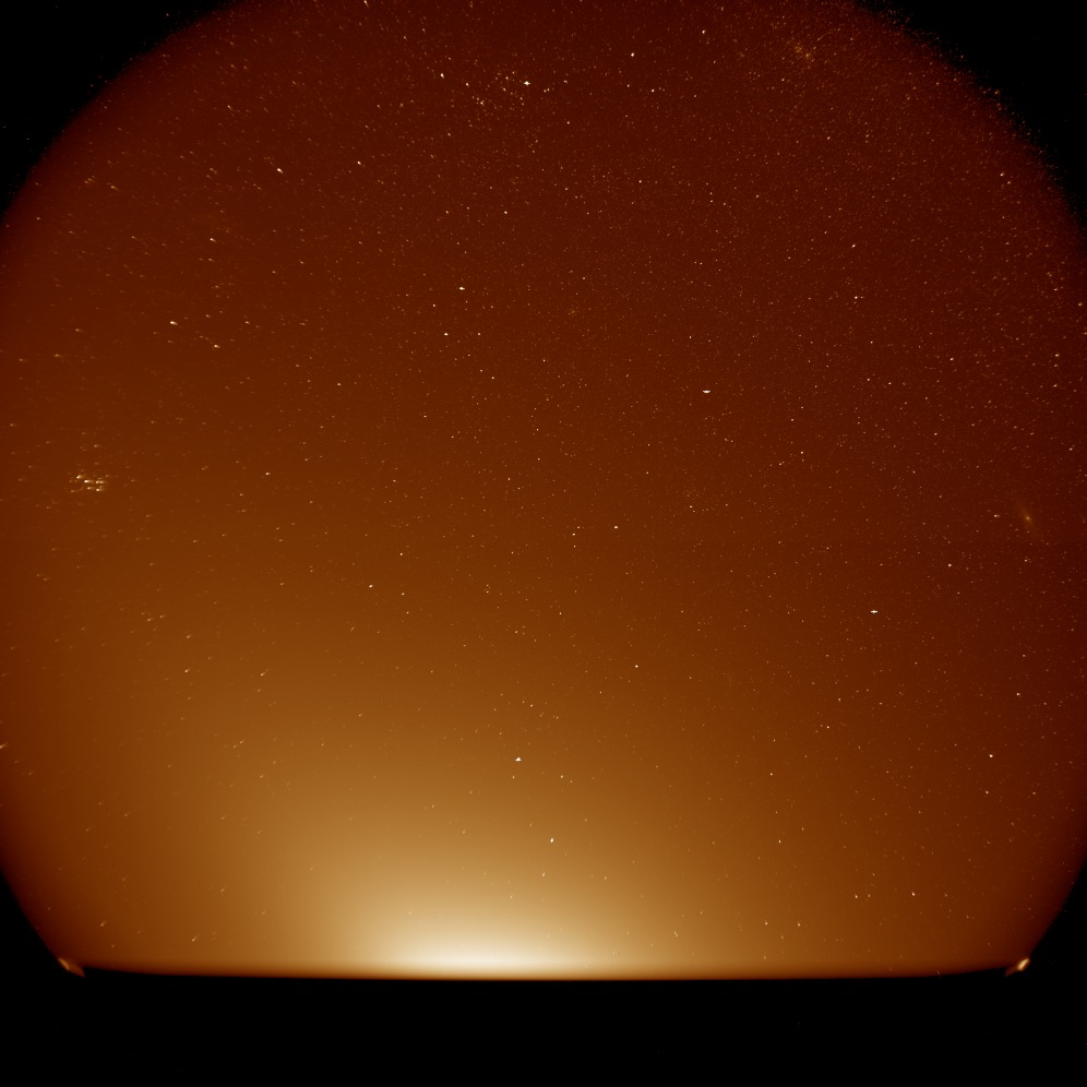 a view of the stars obscured by a diffuse red glow. a wispy cloud is just visible along the right edge