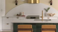 a white kitchen with a curved white backsplash and green emerald tiles on the island