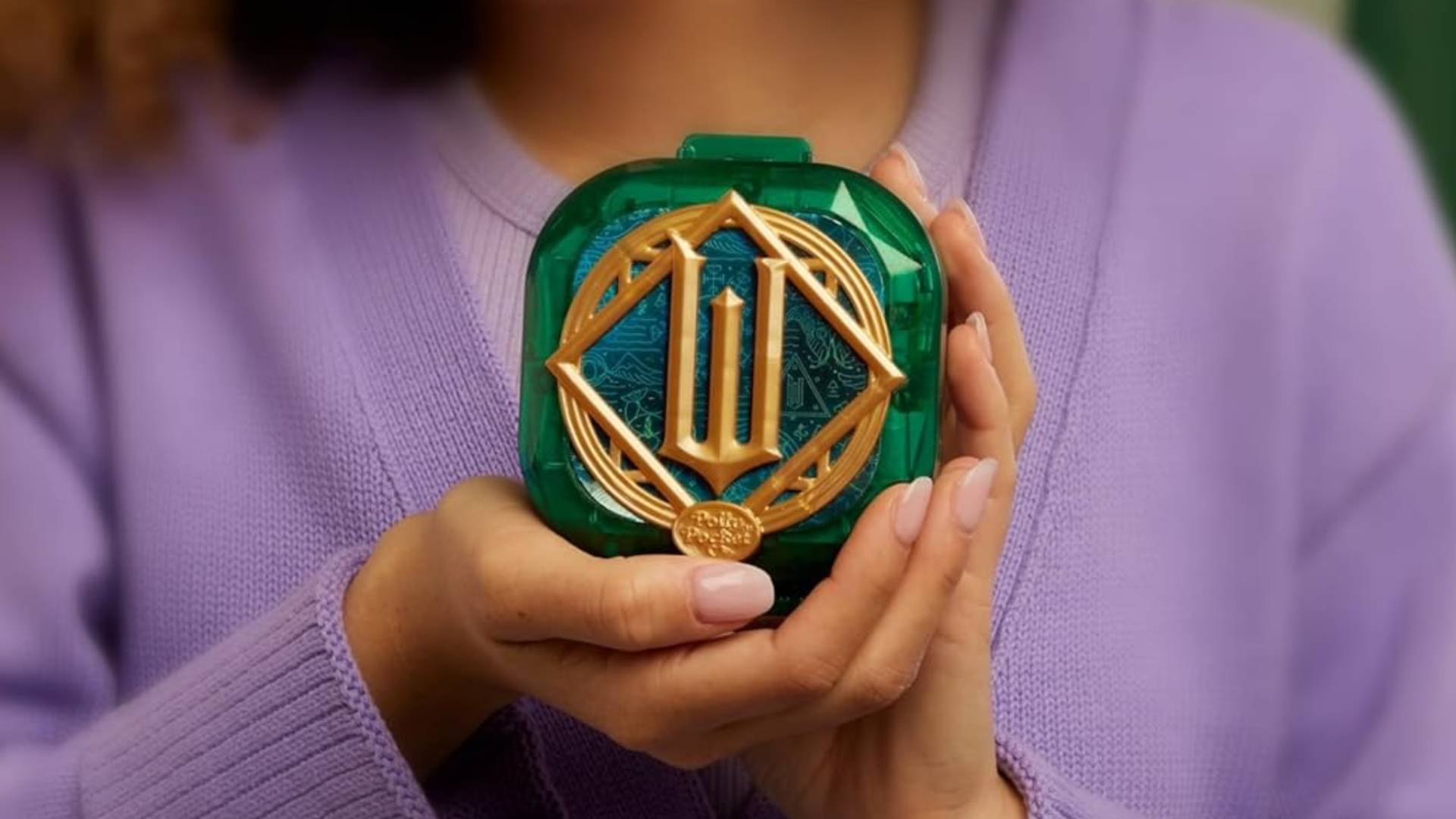 Promotional image for the Mattel Polly Pocket Wicked Compact displaying a child showing the golden 'W' on its exterior.