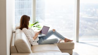 Woman relaxing on a sofa, holding a laptop in her lap and using it