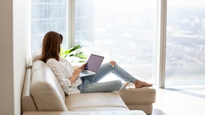Woman relaxing on a sofa, holding a laptop in her lap and using it