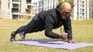 Man practicing walking plank on exercise mat in public park