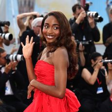 a black woman with long brown hair wearing a strapless red gown on a red carpet in front of a crowd of paparazzi
