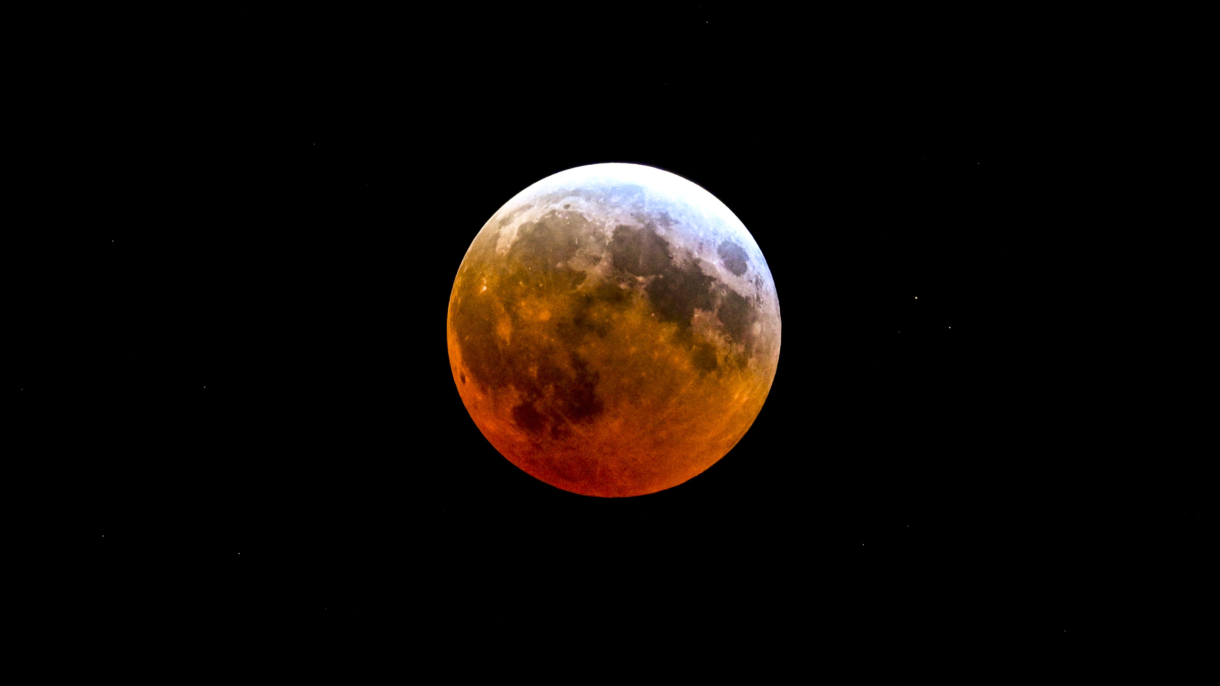 The full moon is photographed in a black sky during a lunar eclipse, with its lower surface glowing red.