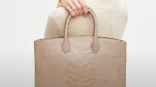 A woman holding a tan leather bag over one shoulder