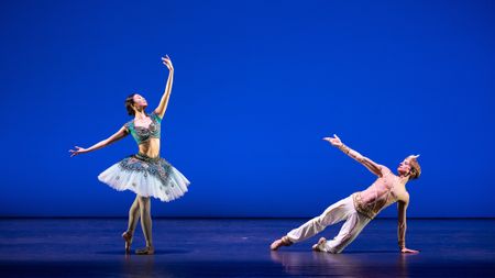 A ballet dancer in a sparkling turquoise costume gracefully poses, while a male dancer stretches in a dynamic lunge on a blue stage