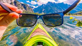 First-person view of sunglasses being put on, sitting in kayak on lake with mountains in the background