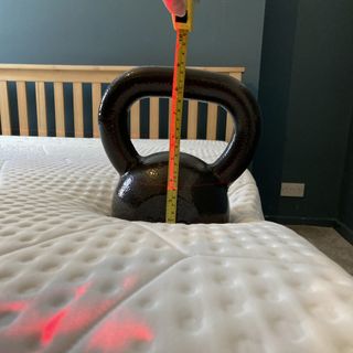 Black kettle bell on a white mattress with a wooden bed frame and a measuring tape