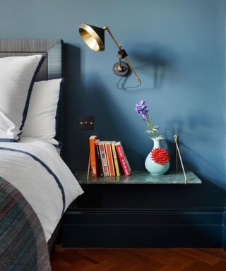 A blue bedroom with rich dark wooden floor, bedside table and brass wall lights.