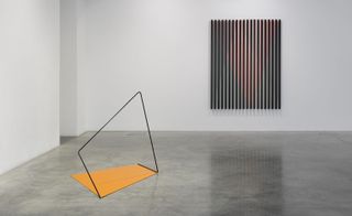 Rana Begum's gallery space, white walls, grey gloss marble floor, angular black frame and yellow piece artwork on the floor, metal artwork piece on the far wall