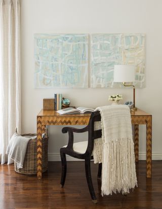 home office with polished hardwood floor, inlaid desk, blanket, artwork, lamp, basket