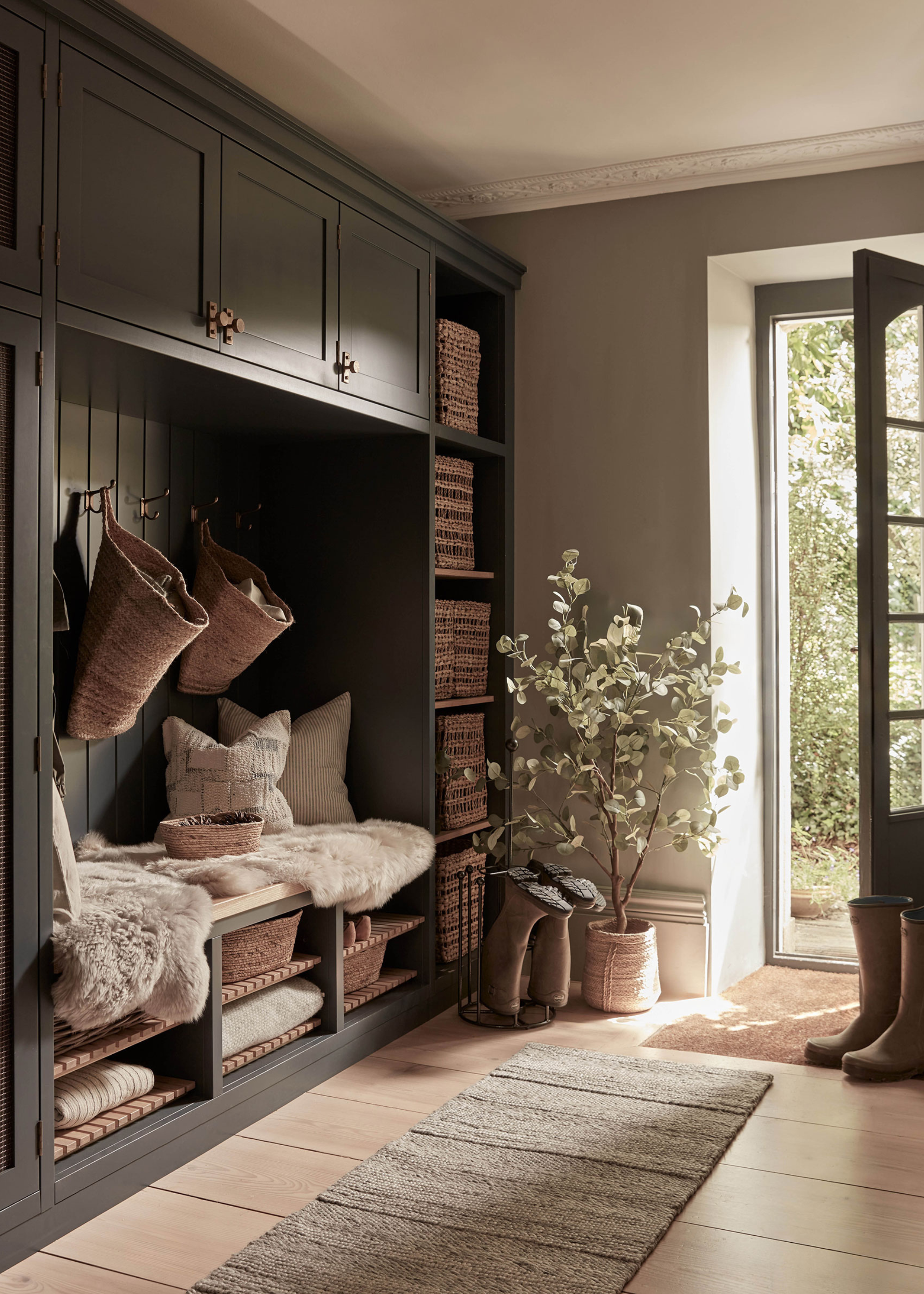 painted grey hallway built-in closet with hanging storage baskets, wicker baskets on shelves, built-in seating and an open glass door with a plant next to it