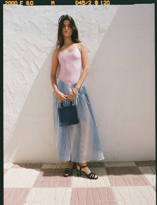 a model stands in front of a whitewashed wall wearing a swimsuit and irridescent skirt