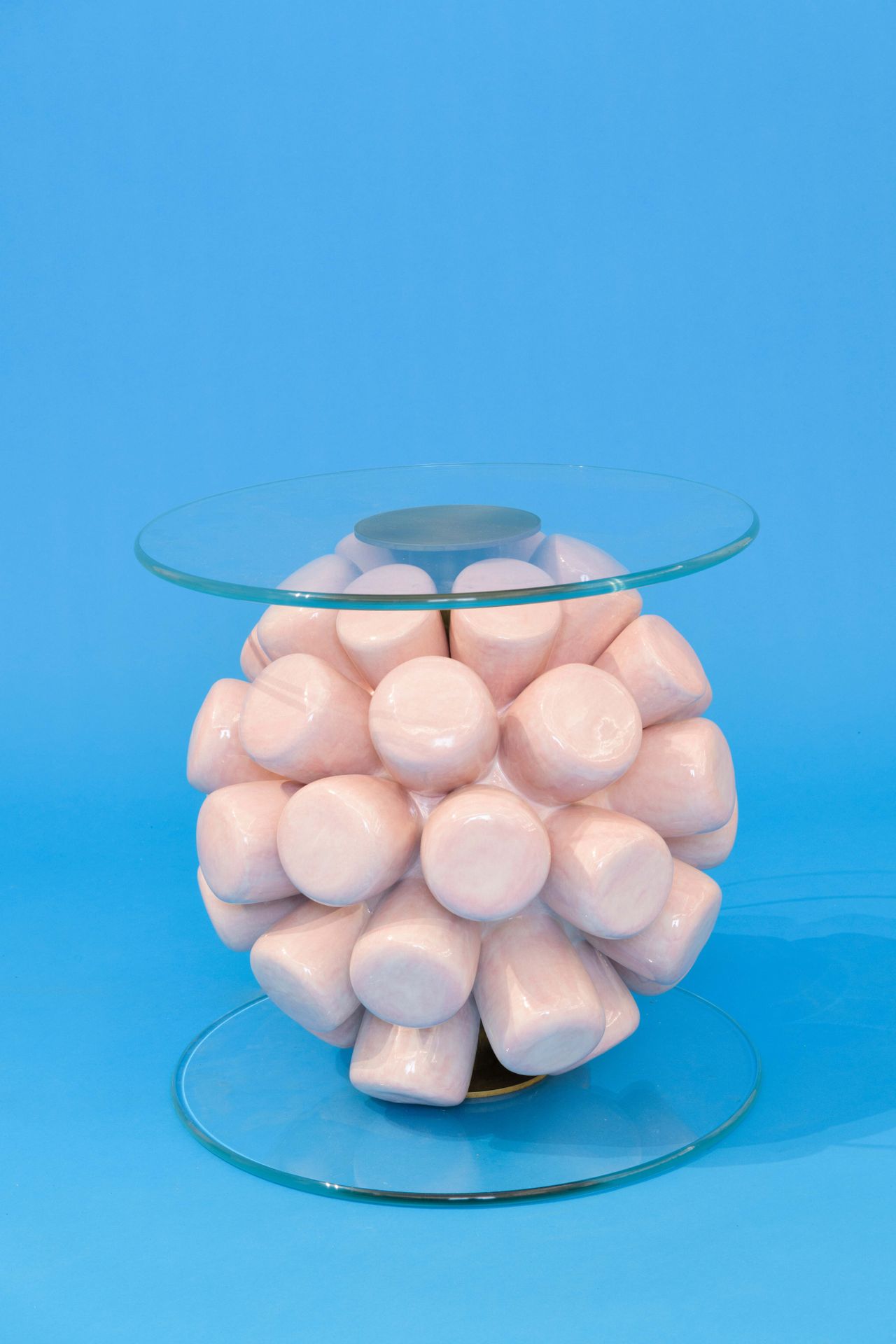 A side table of a ball of handmade ceramic marshmallows sandwiched between two circular planes of glass.