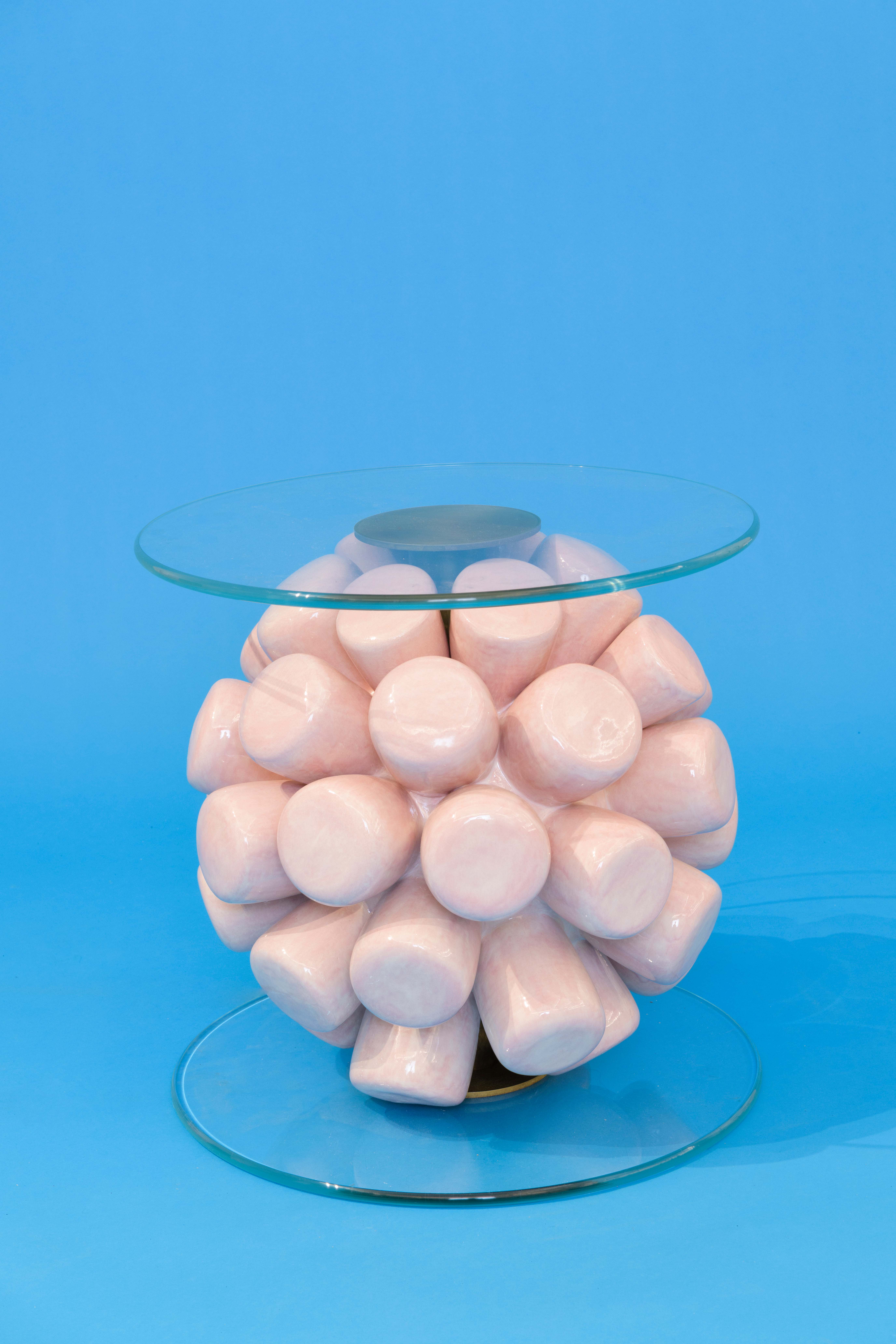 A side table of a ball of handmade ceramic marshmallows sandwiched between two circular planes of glass.