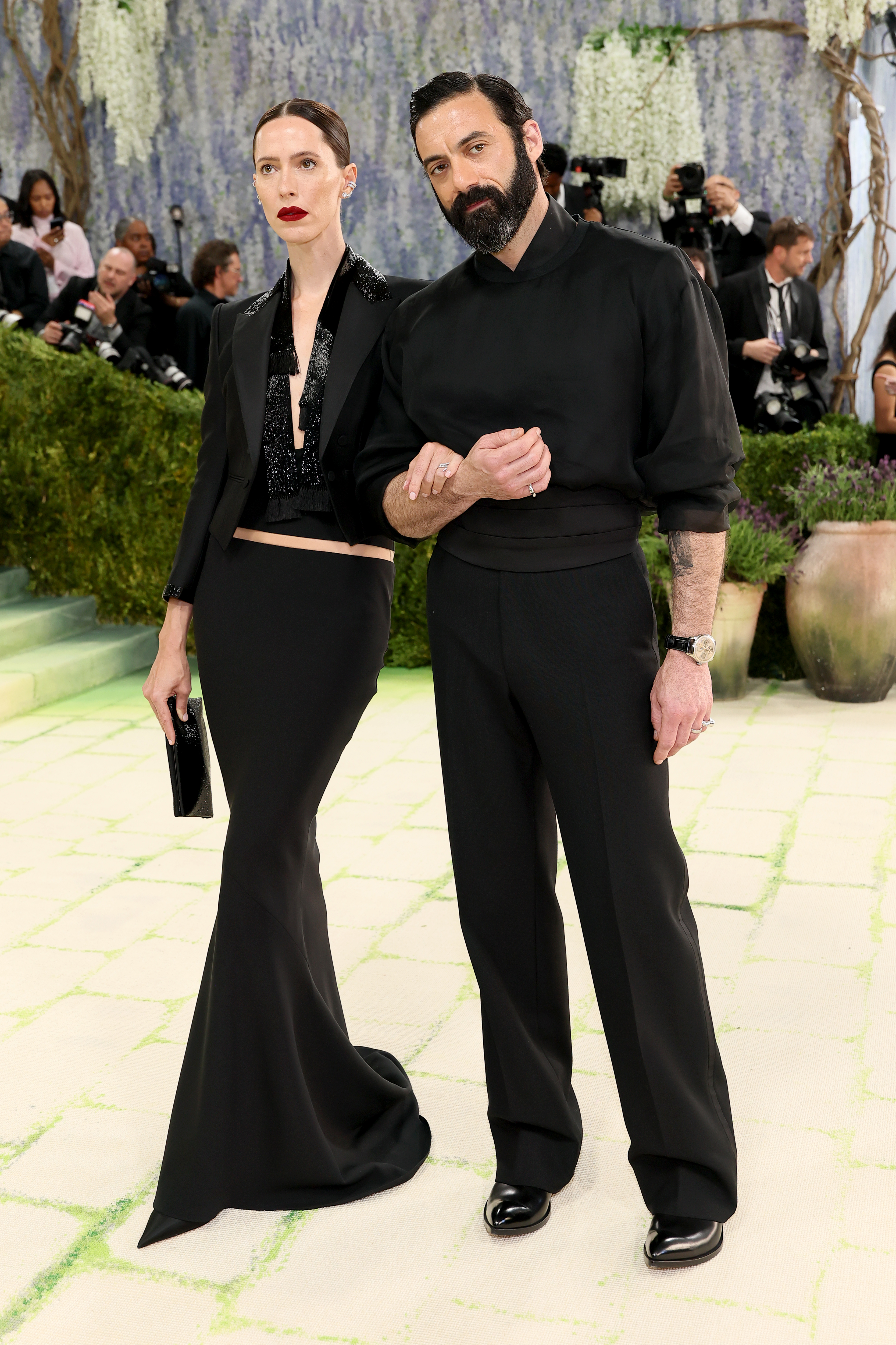 a women in a black shirt and skirt standing on a cream carpet next to a man in black pants and black shirt