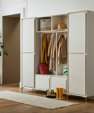 An entryway with a white cupboard with coats, hats, shoes, and storage baskets