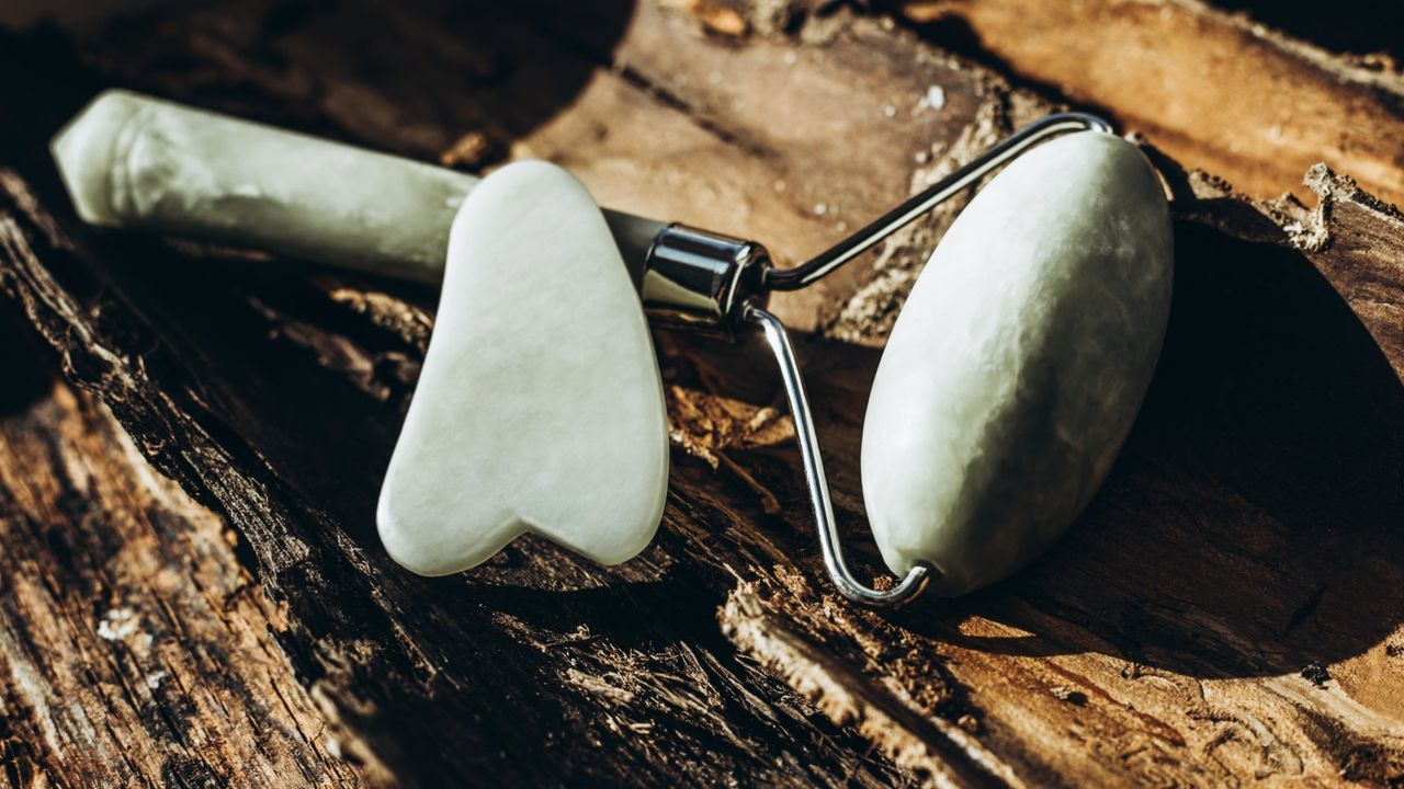 A jade roller and a guache scraper lie on the bark in the rays of the bright sun with place for text.