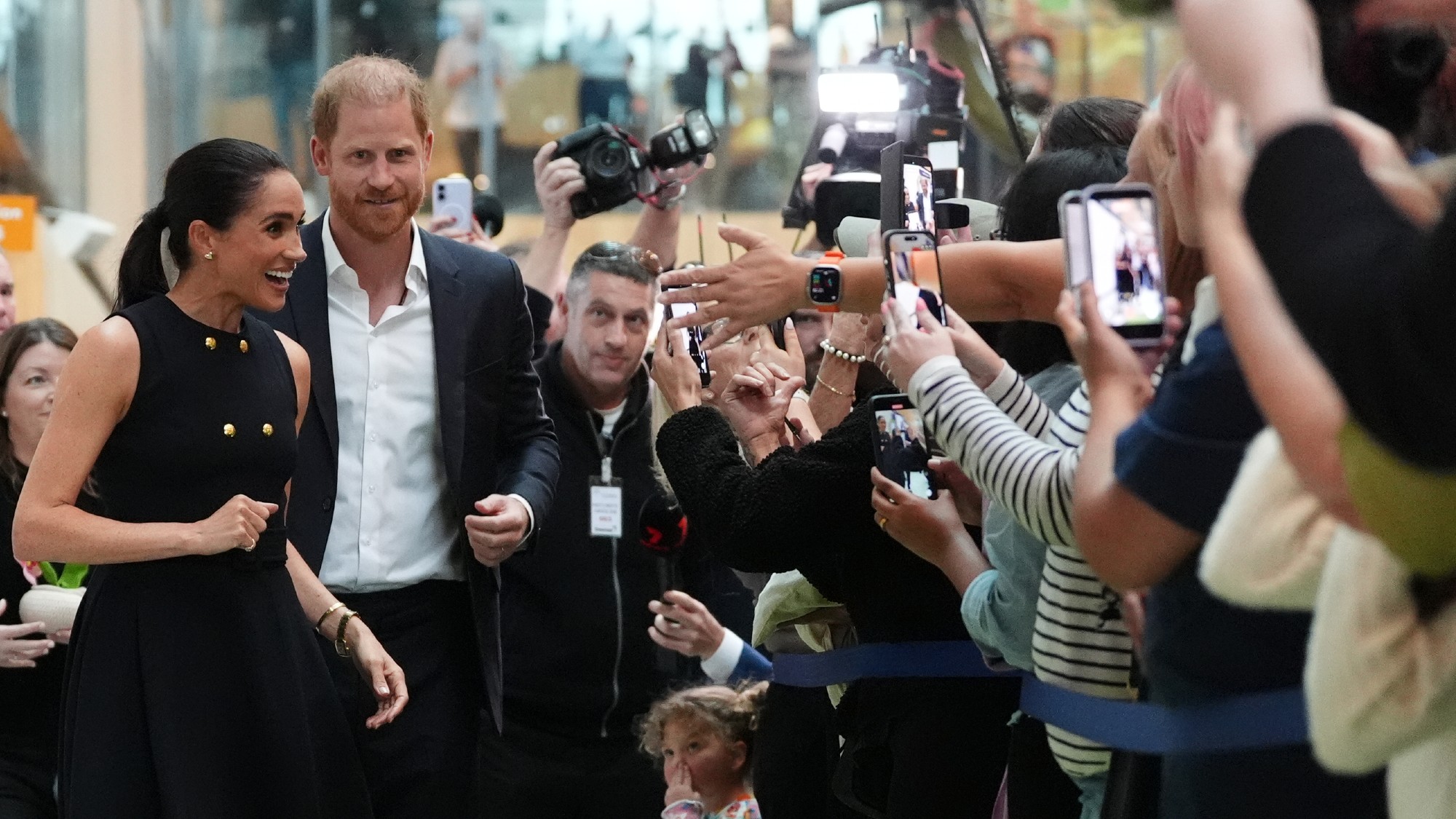 Meghan, Duchess of Sussex and Prince Harry, Duke of Sussex walk by photographers and spectators taking pictures with smartphones on a visit to the Royal Children's Hospital in Melbourne