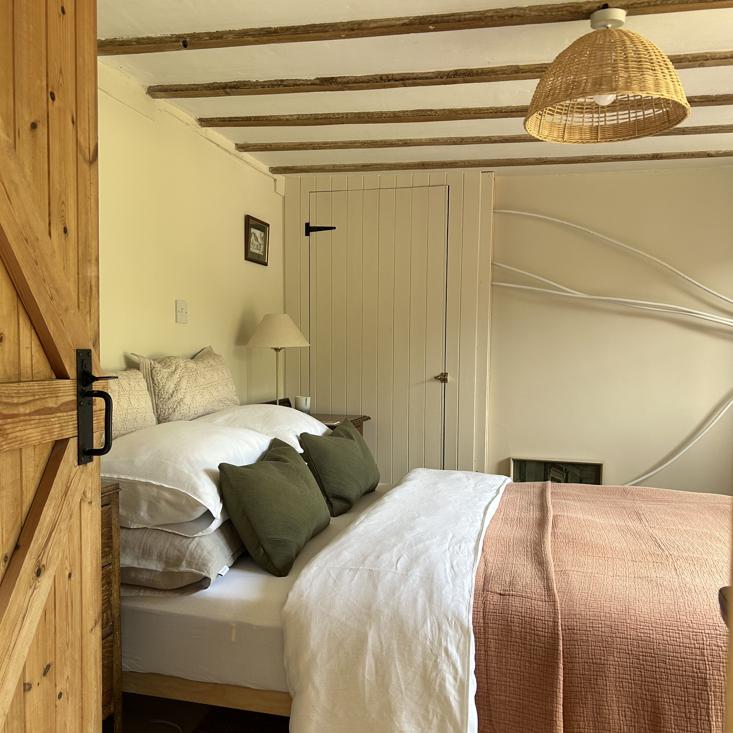a bedroom with a beautifully-made bed even though wires still hang on the wall next to it mid renovation