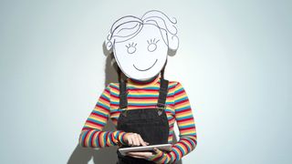 Portrait of a young woman wearing homemade cardboard mask and using a digital tablet on a light blue background