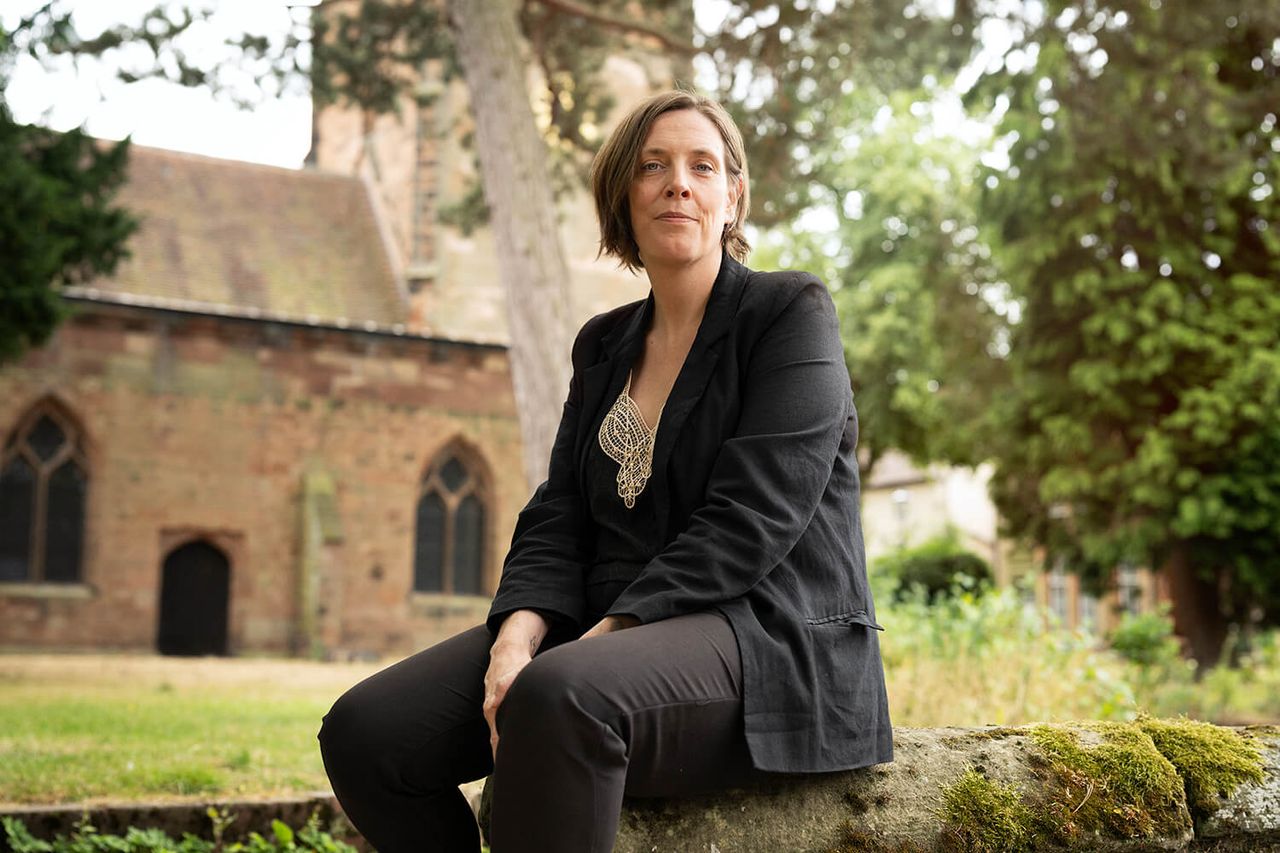 Woman wearing suit sat on wall. Church in background.