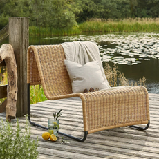 George Home rattan garden lounge chair next to a lake.