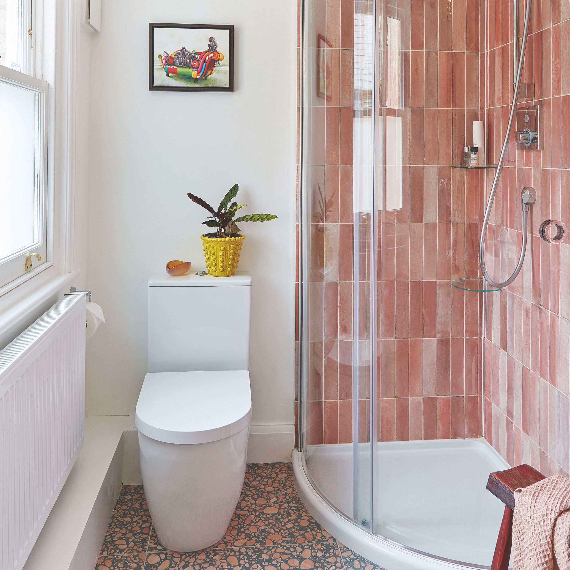 White painted bathroom with a toilet next to a semi-circular shower cubicle decorated with pink tiles