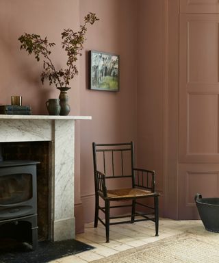 light brown living room with marble fire surround, log burner, vases, artwork, black wood and cane chair, floorboard, rug