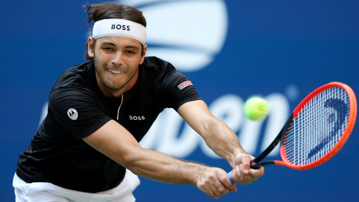 Taylor Fritz stretches for a backhand at the U.S. Open 2024 in a black t-shirt, white shorts and Hugo Boss headband.