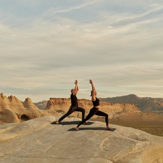 Two people practice yoga on a stone mountain range.