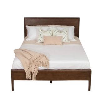 A walnut bed frame with a mattress, pillows, and throws on it