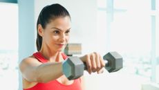 A woman in a tank top performs a lateral raise with a dumbbell. She holds the dumbbell in her right hand and her arm is straight out at shoulder height. 