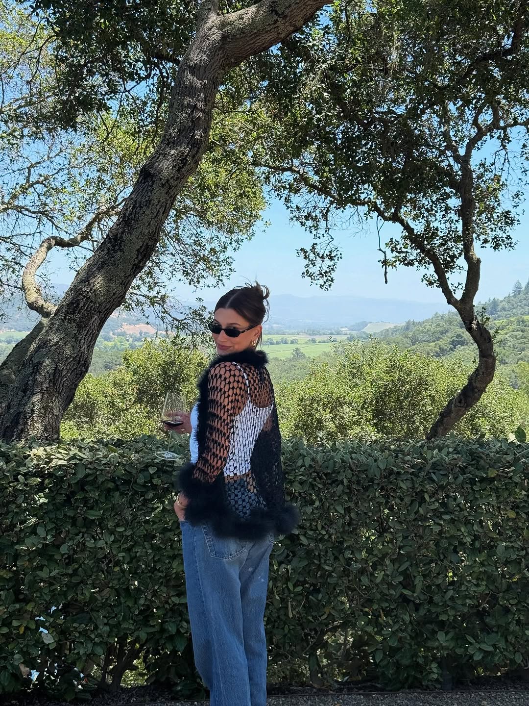 Hailey Bieber denim outfit jeans and white tank top with black fishnet cardigan 2025