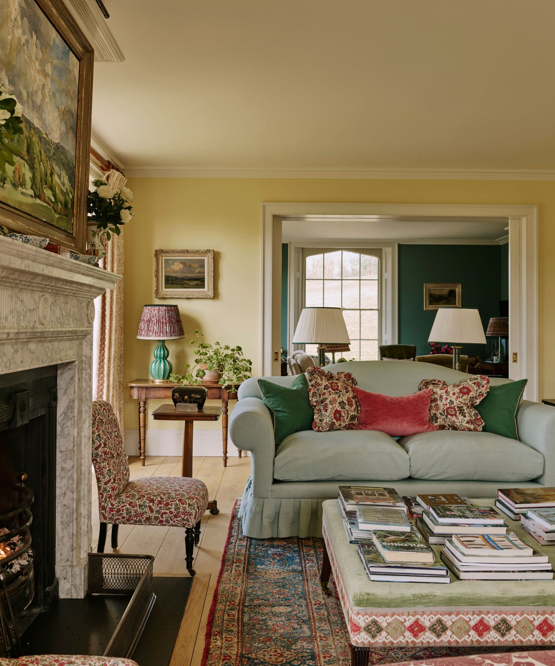 elegantly styled living room featuring a light blue skirted sofa with colorful accent pillows, a marble fireplace, an upholstered coffee table stacked with book