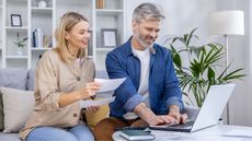 A couple do financial planning while sitting on the sofa, a laptop on the table in front of them.