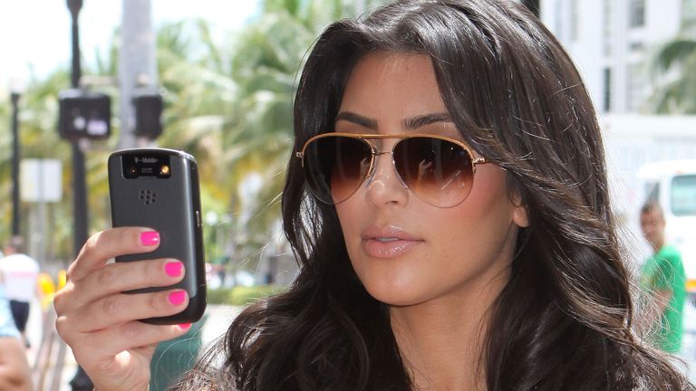 Kim Kardashian holding a BlackBerry mobile phone up to eye level.