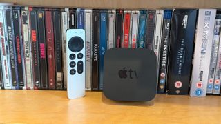 Apple TV 4K on a shelf with Blu-ray cases behind