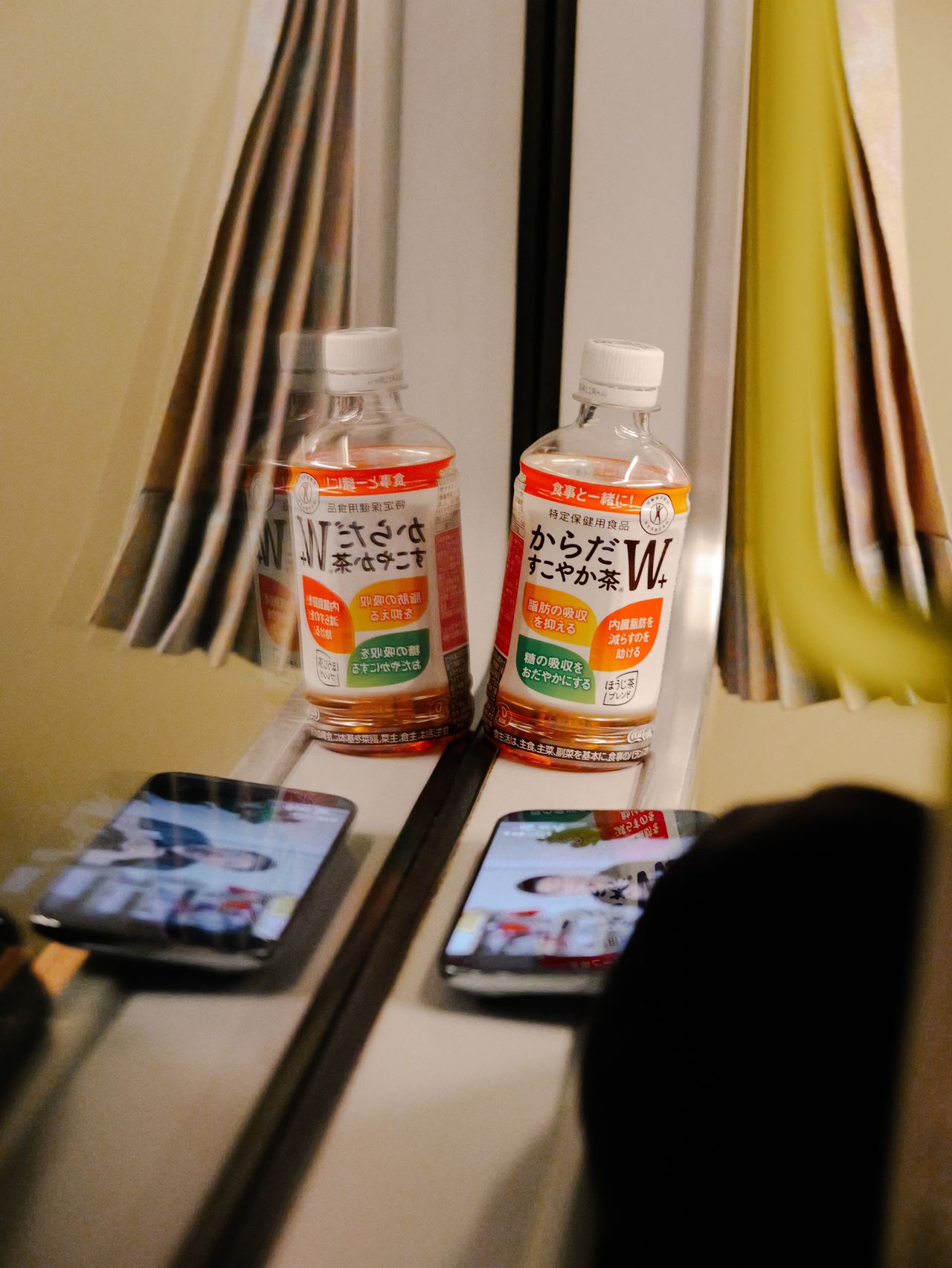 Bottled tea and smartphones reflected in a train window.