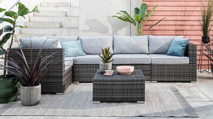 Best rattan garden furniture - a rattan corner sofa on a paved patio with concrete steps behind