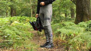 A model wearing the Renen MTB Pant on a trail lined by ferns