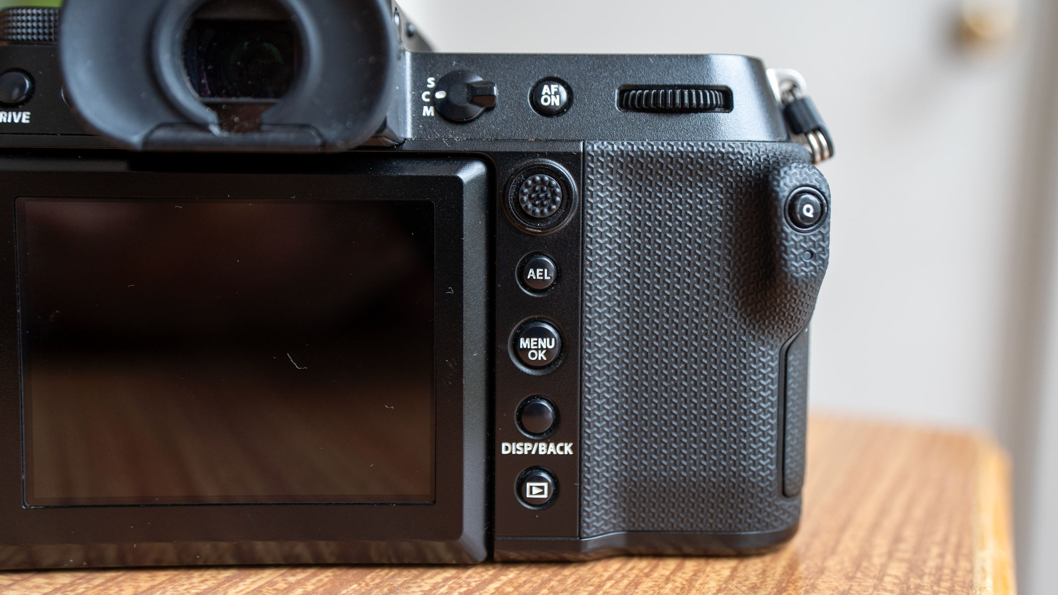 The back panel of the Fujifilm GFX100S II showing button, dials, and grip on a wooden table.