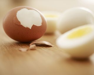 A hard boiled brown-shelled hen's egg with partially-cracked shell, next to sliced hard-boiled egg