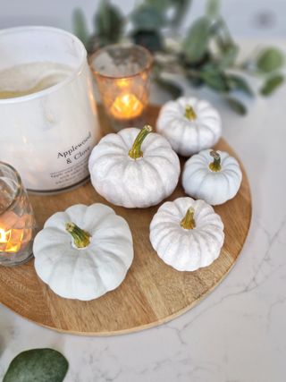 A selection of decorative pumpkins painted white with gold stalks next to a candle