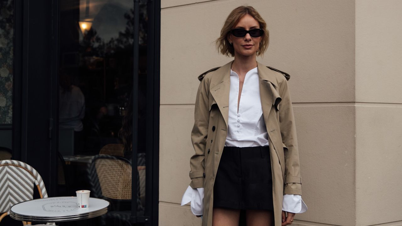 paris fashion week spring 2025 attendee wearing trench coat black skirt sunglasses and white button down shirt 