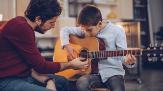 Man shows boy how to play the acoustic guitar