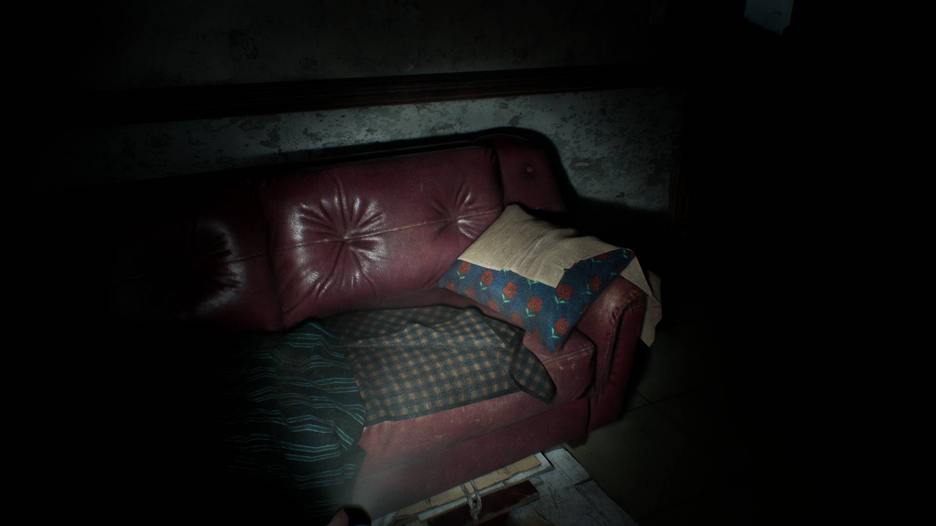 Resident Evil Requiem screenshot of flashlight reflecting on red leather couch.