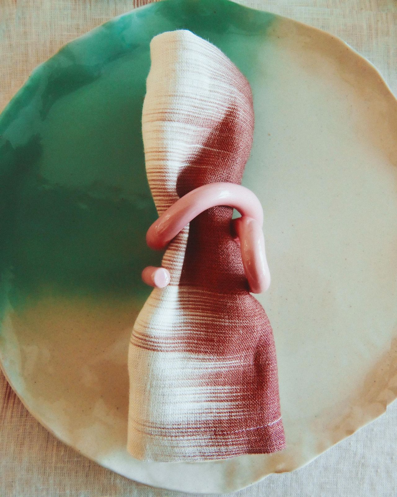 Close-up image of a white and teal plate with a red and white napkin on it and a light pink napkin ring around the napkin.